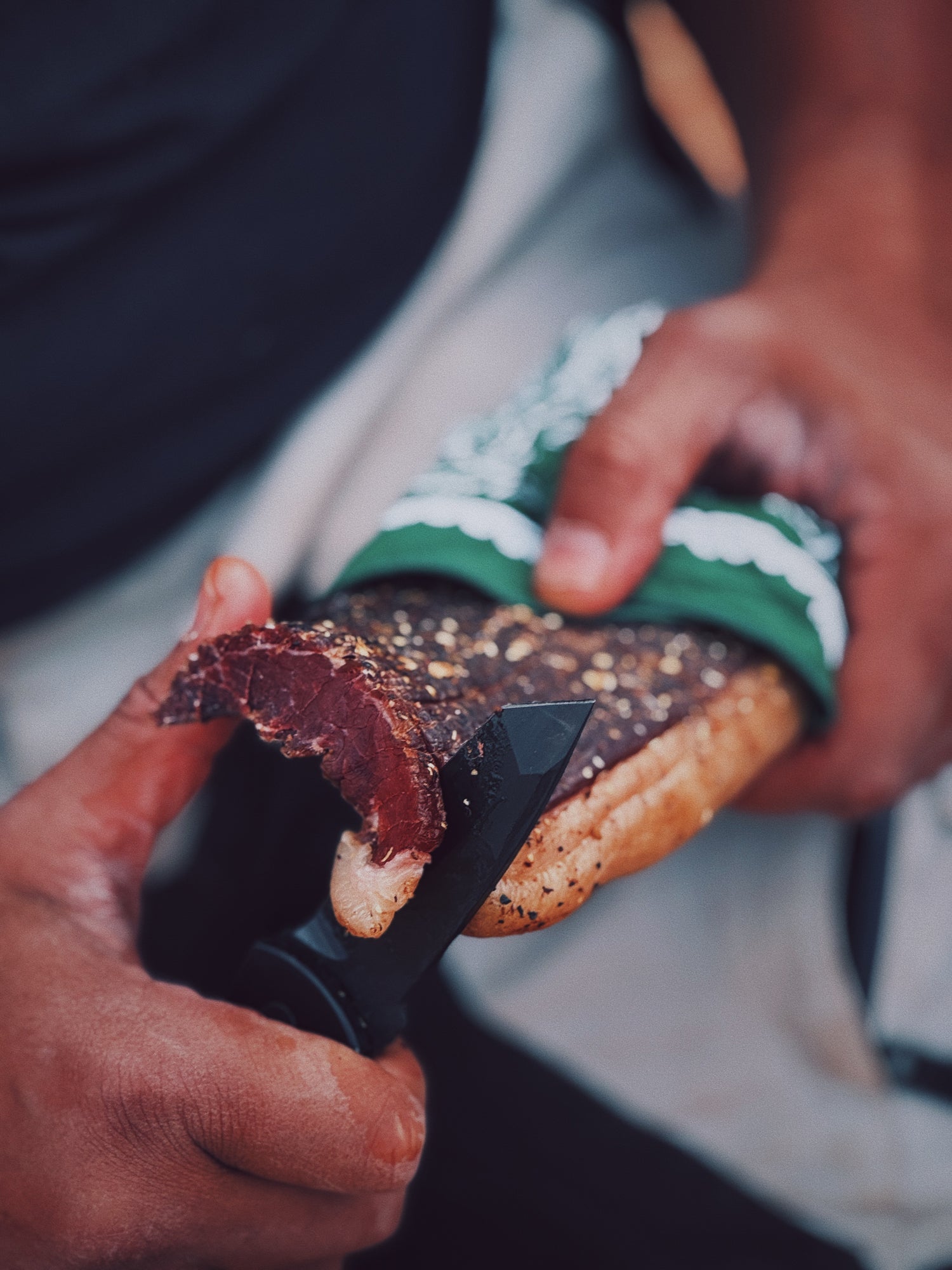 Person slicing a whole grass-fed biltong slab wrapped in a green and white bandana.