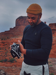 Man holding a black and white Brave Bandana in a desert landscape with red rock formations.